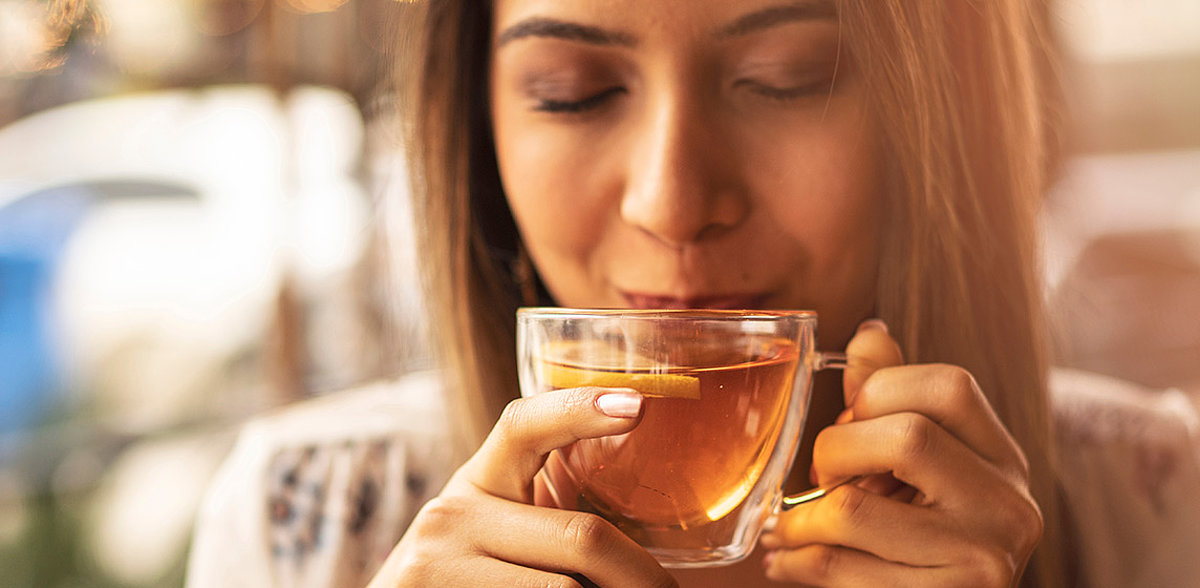 Junge weibliche Person trinkt Tee aus einer Glastasse